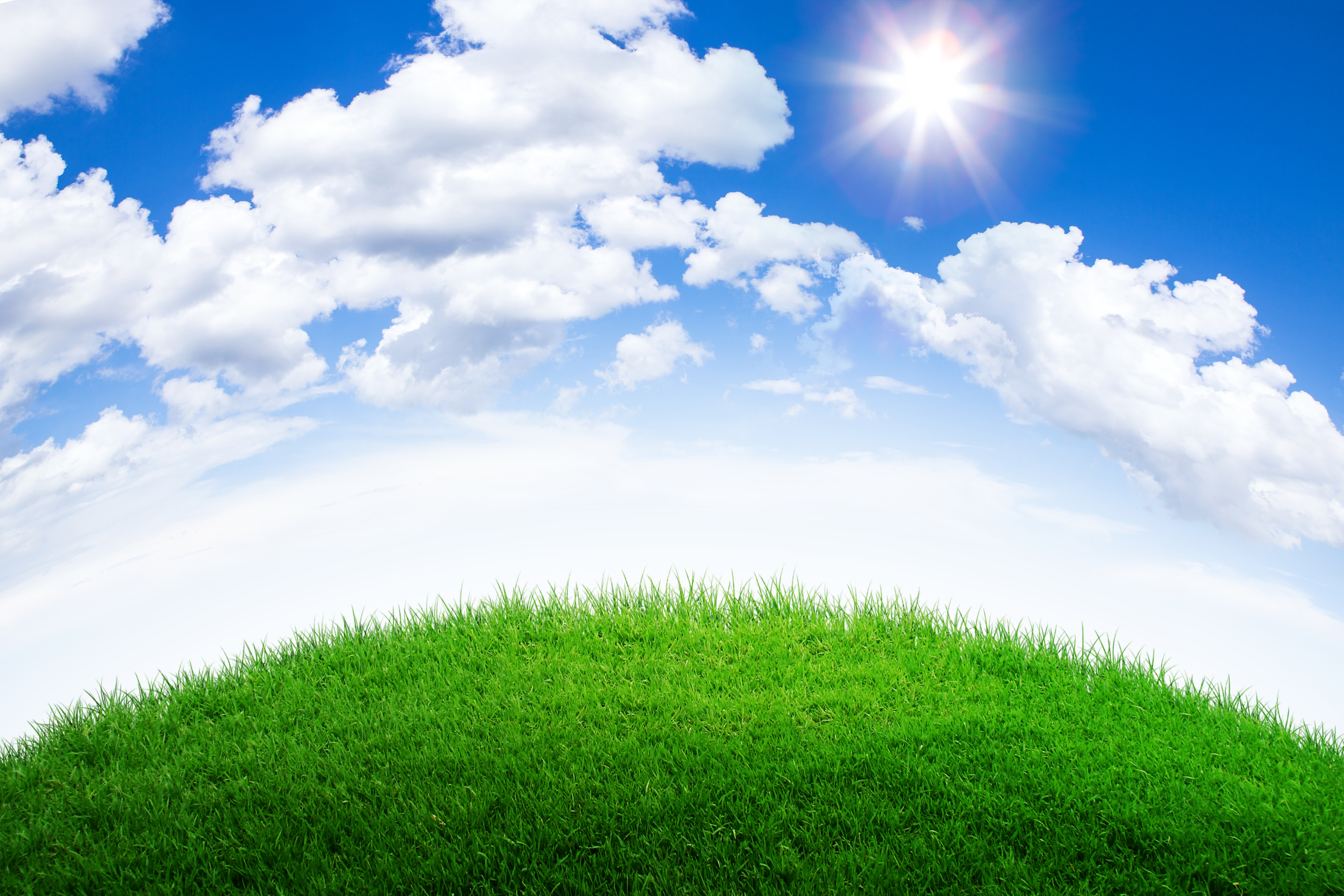 a green grass hill with blue sky and clouds