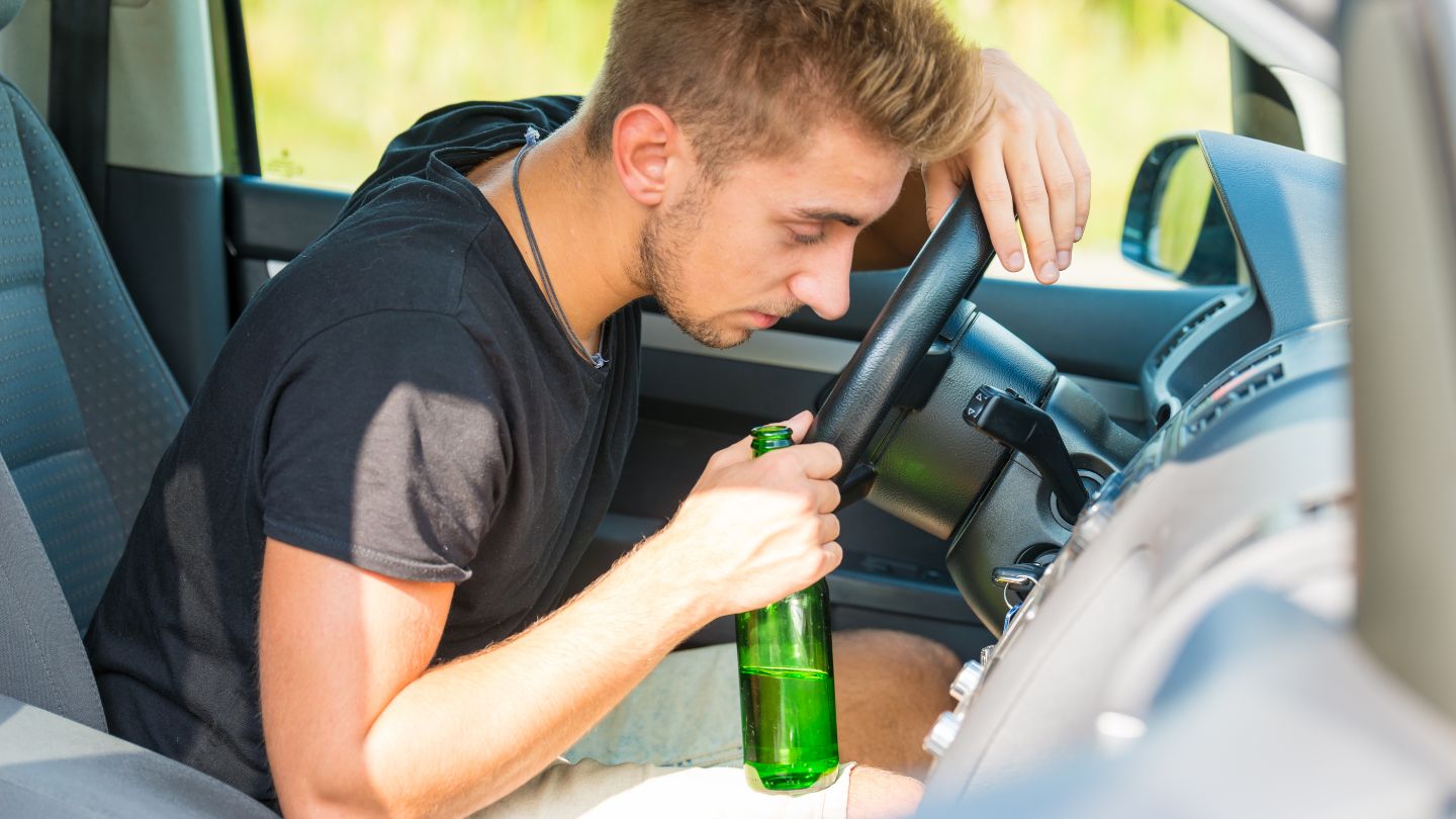 a man holding a bottle of beer while driving