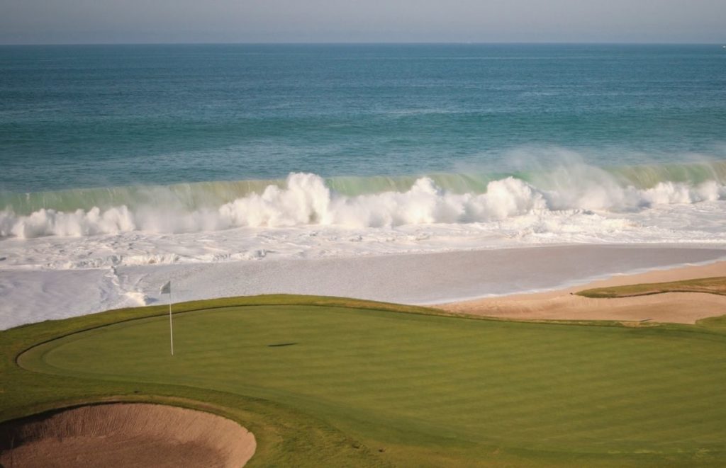 a golf course with a large wave crashing on the beach