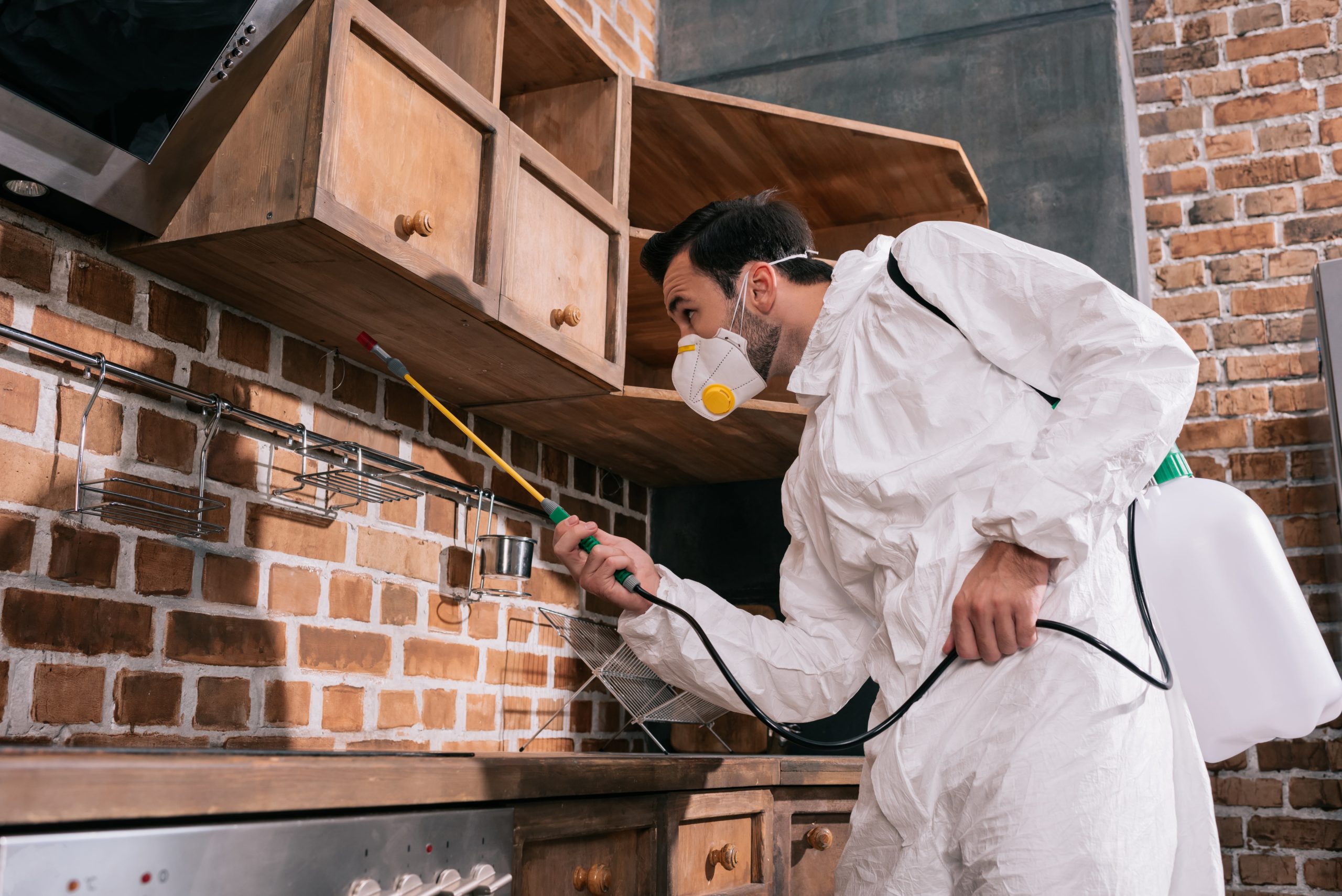 a man wearing a white suit and mask spraying a kitchen