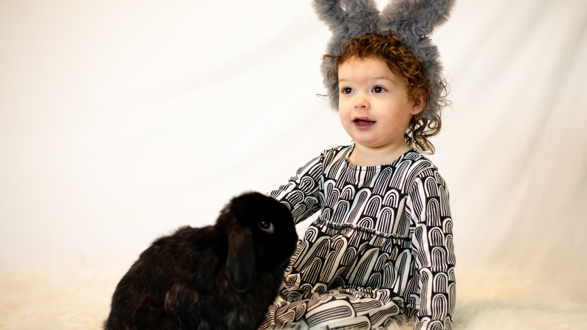 a child wearing bunny ears and sitting next to a black rabbit