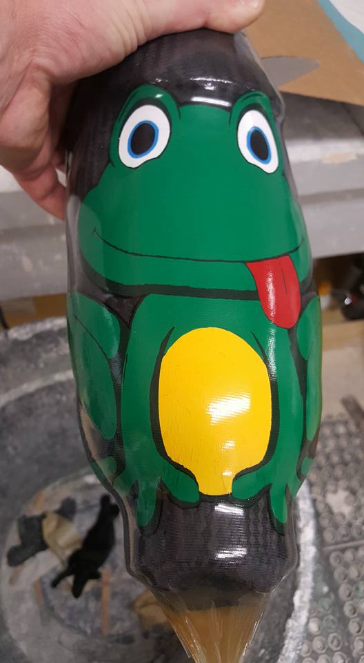 a hand holding a green bottle with a cartoon frog on it