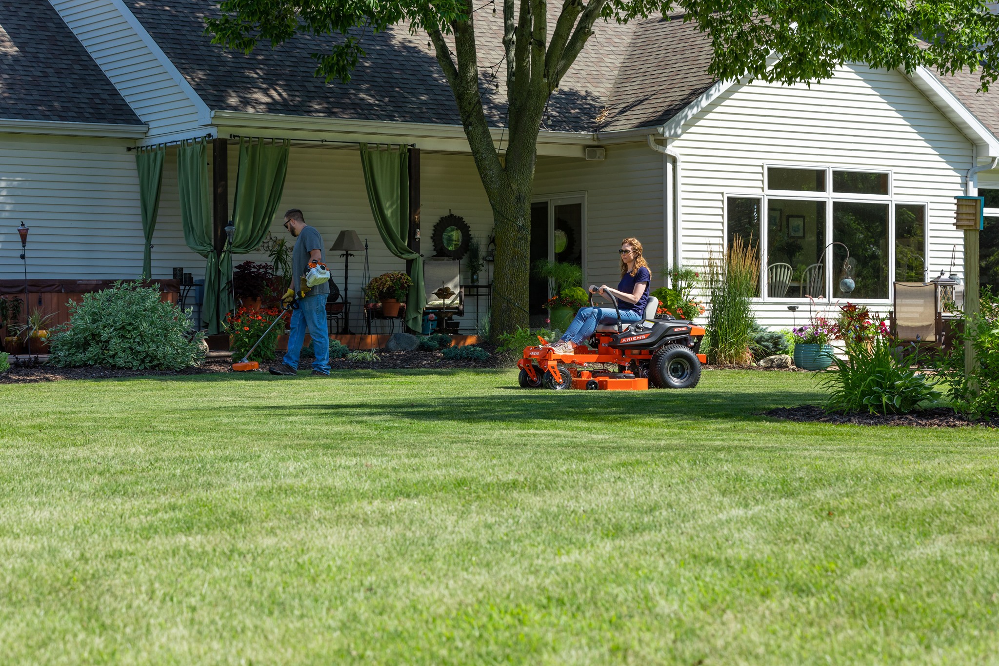 a man and woman riding a lawnmower in a yard