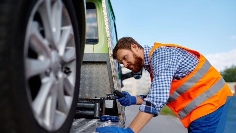 a man in an orange vest looking at a tire on a truck