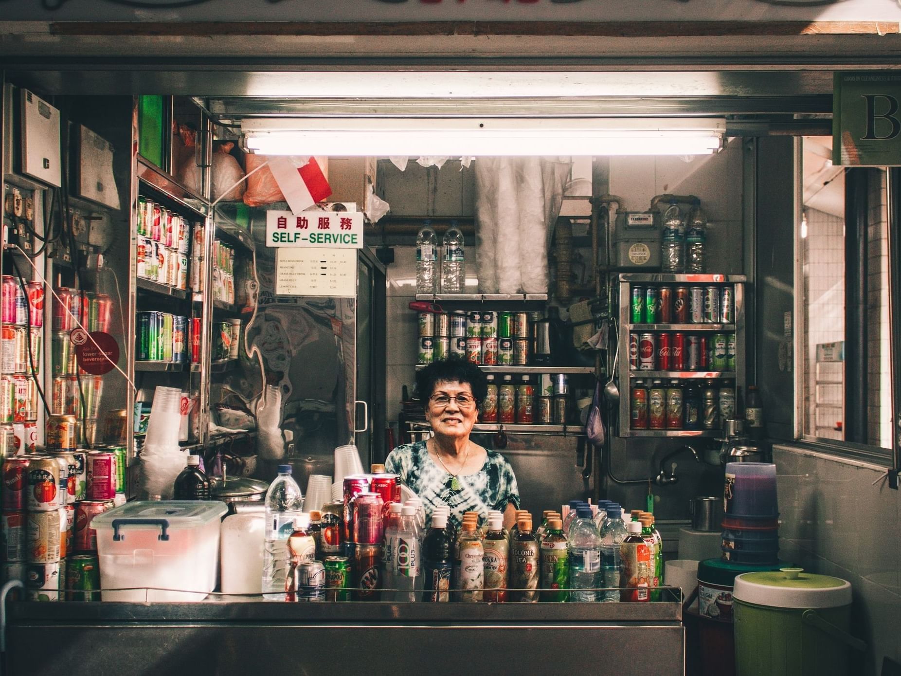 a woman behind a counter with bottles of soda and other beverages