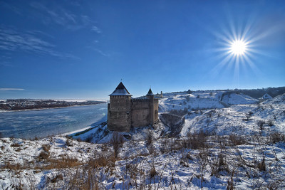 a castle on a hill with snow and a body of water