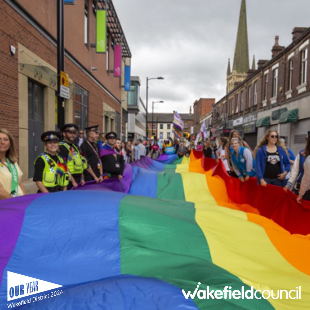 a group of people walking down a street with a large rainbow flag