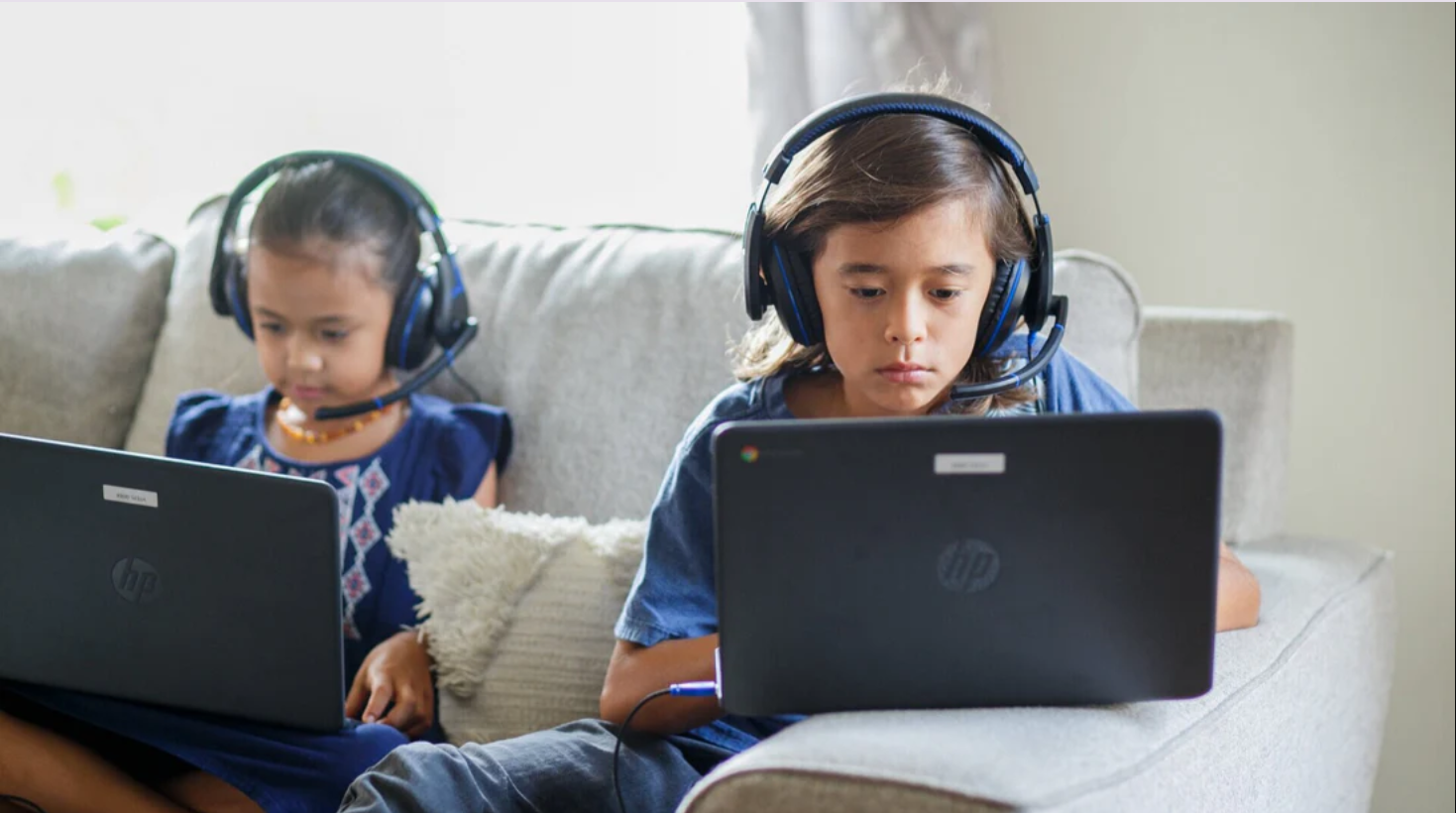 a couple of children sitting on a couch using laptops