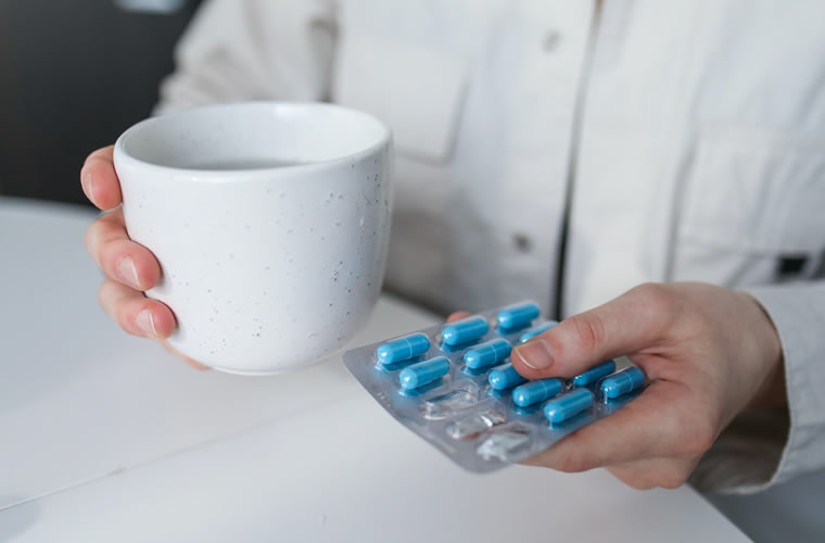 a person holding a cup and a blister of pills