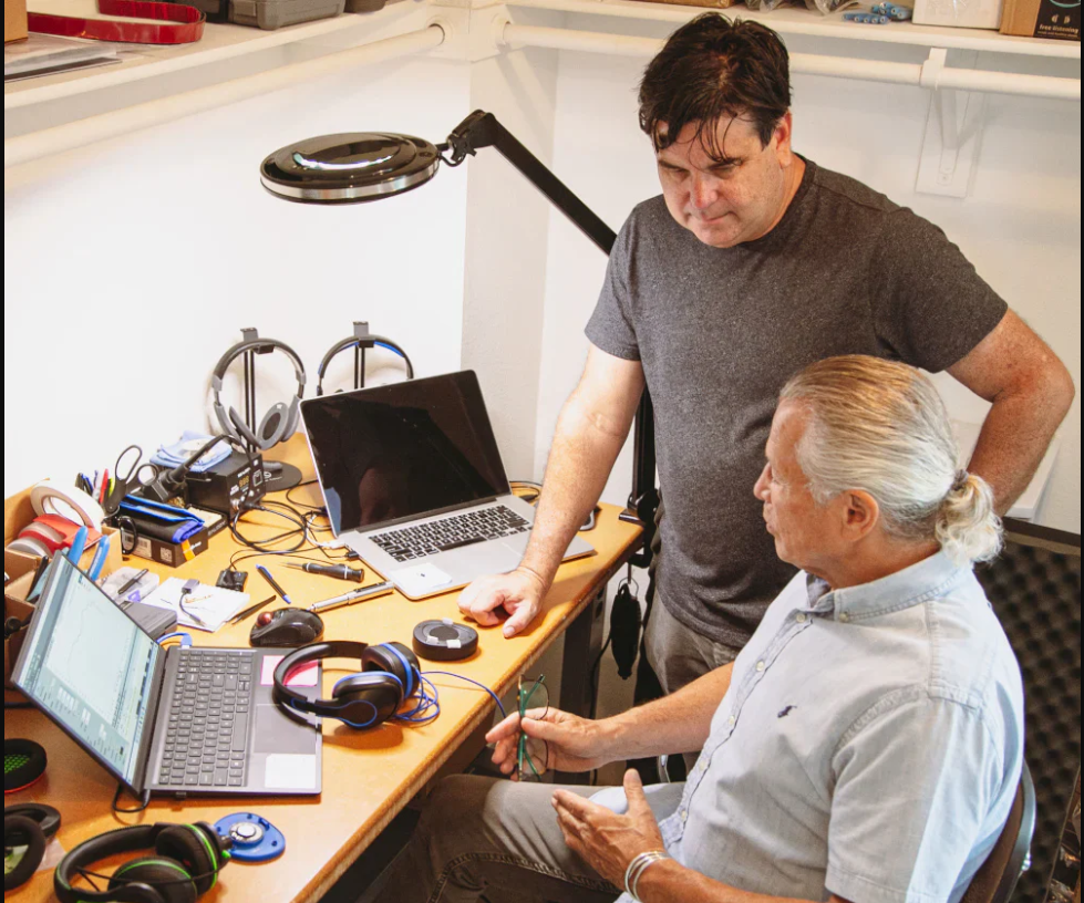 a man standing next to a man sitting at a desk with a laptop