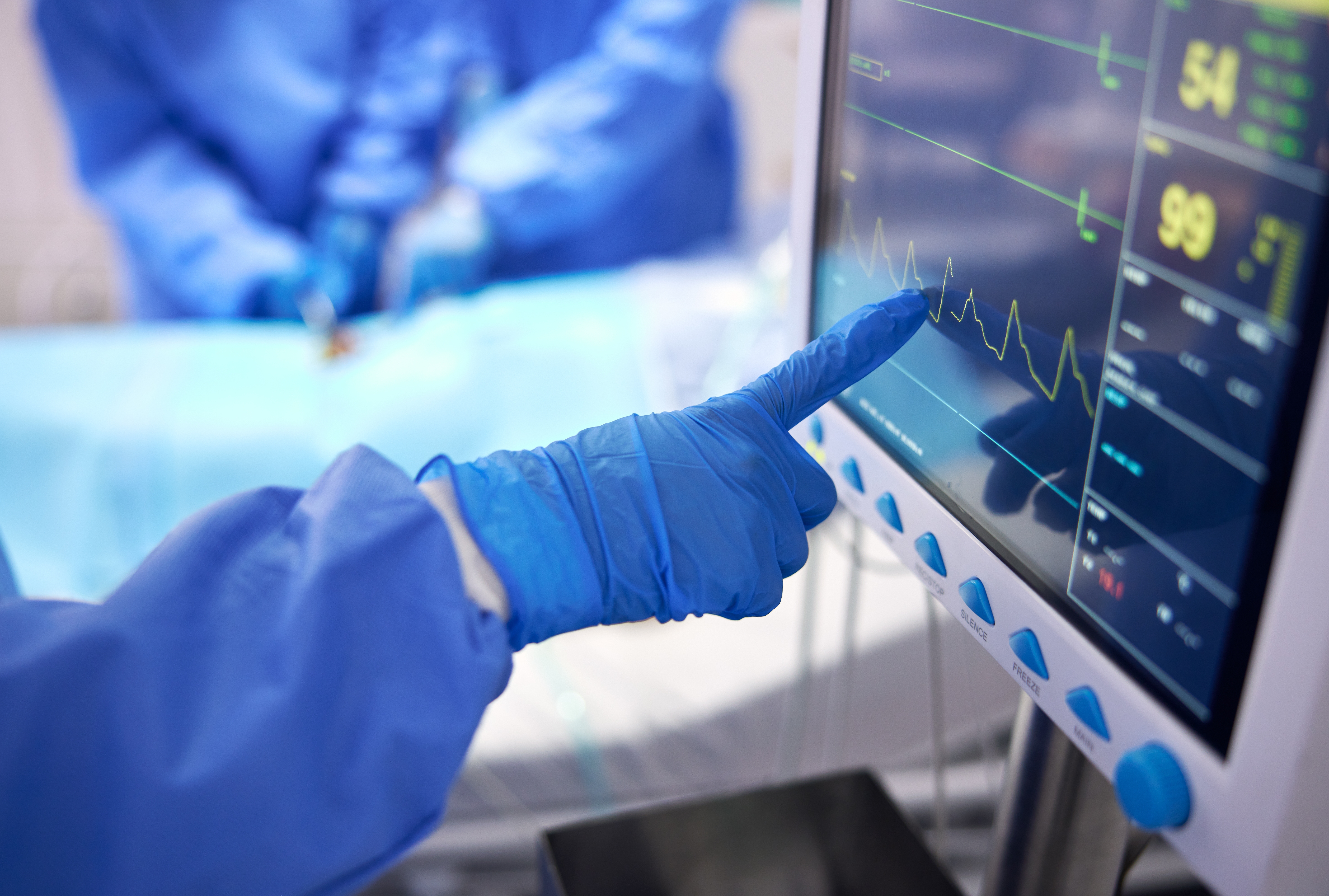 a person wearing blue gloves pointing at a monitor